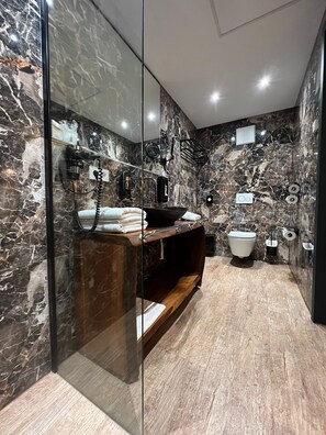 A modern bathroom with a marble backsplash, a glass shower enclosure, a wooden vanity, and a toilet. - Hotel Winterrot (Karlsruhe)