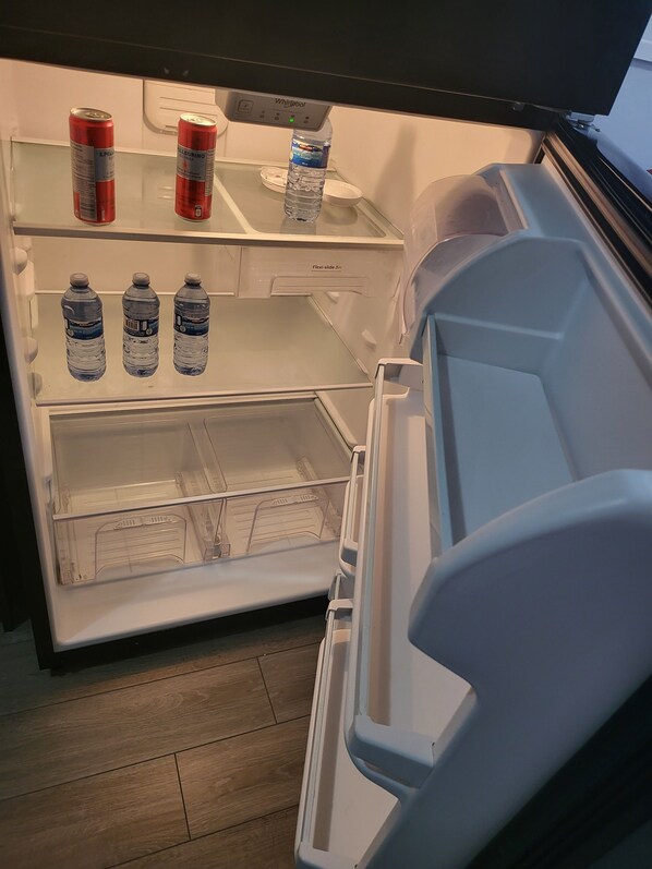 Un refrigerador abierto con un dispensador de agua, dos latas de Pelle y tres botellas de agua.