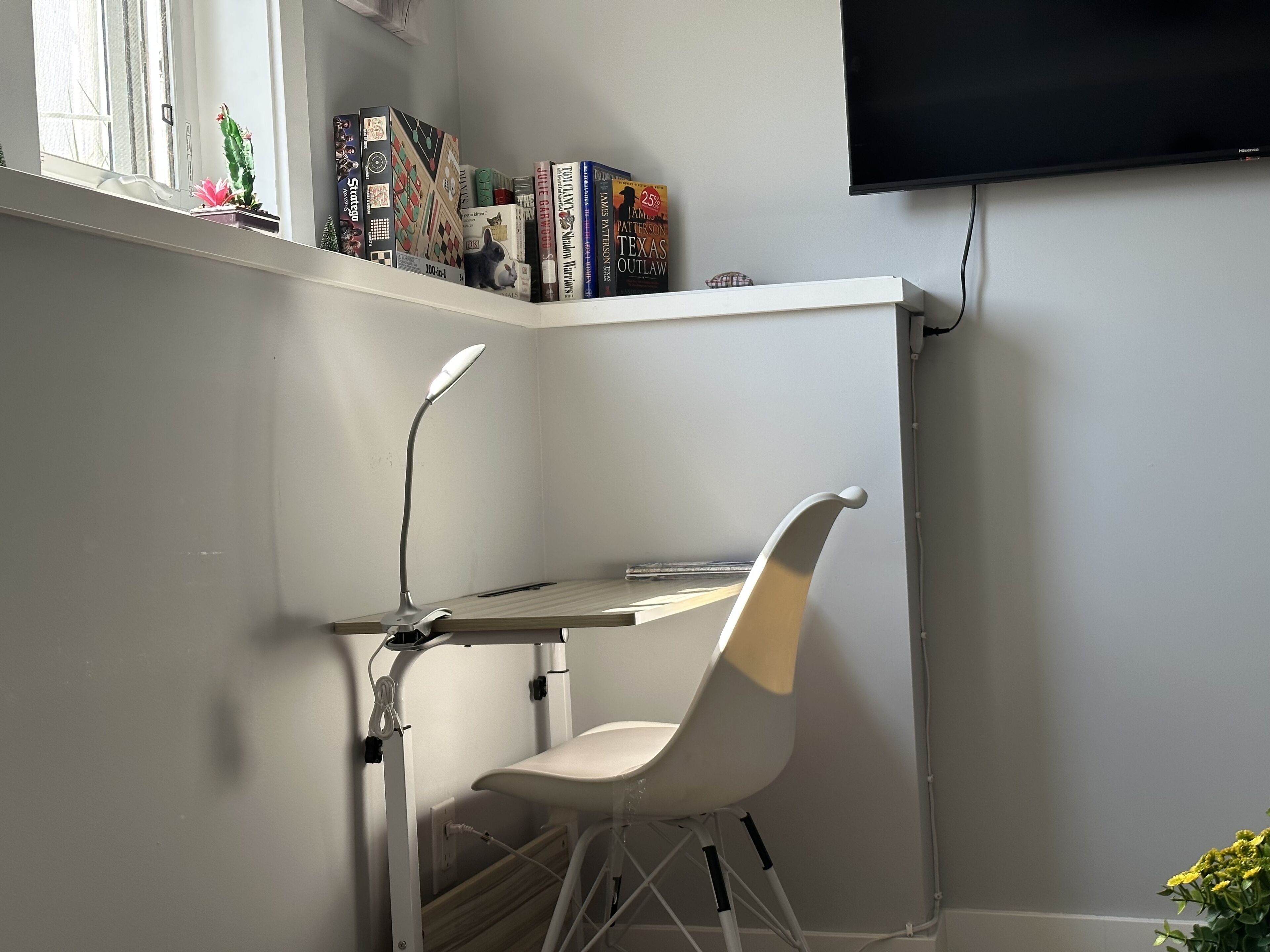 Ein Arbeitsplatz in der Ecke mit einem weißen Schreibtisch, einem weißen Stuhl, einer Stehlampe und einem Bücherregal mit Büchern und Dekoration.