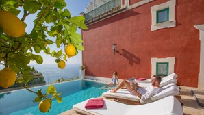 A poolside area with lounge chairs and a red building in the background. - Villa Aurora in Praiano (Praiano)