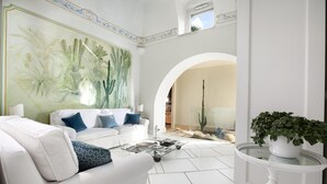A modern living room with a white sofa, a glass coffee table, and a large botanical mural on the wall. - Villa Aurora in Praiano (Praiano)