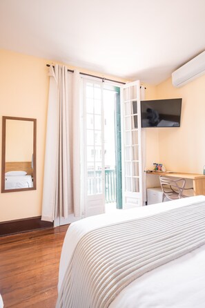 A hotel room with a bed, a desk, a chair, a TV, and a balcony with curtains. - Pousada Catedral (Petrópolis)