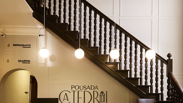 Un comptoir d’accueil avec une façade en pierre, un escalier avec des balustrades noires et des panneaux indiquant l’emplacement du restaurant et des chambres.