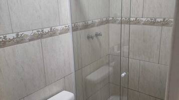 Een kleine, afgesloten douchecabine met een glazen deur, een toilet en een douchekop.