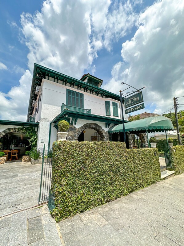 A building with a sign reading "POUDA ATEODRIL" and a phone number. There is a green awning and a stone archway. - Pousada Catedral (Petrópolis)