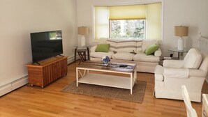 Un salon avec un téléviseur à écran plat posé sur un meuble en bois, un canapé, une table basse et deux lampes.
