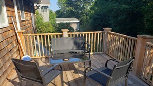 Une terrasse en bois avec une table et des chaises en métal, entourée d’une balustrade en bois.