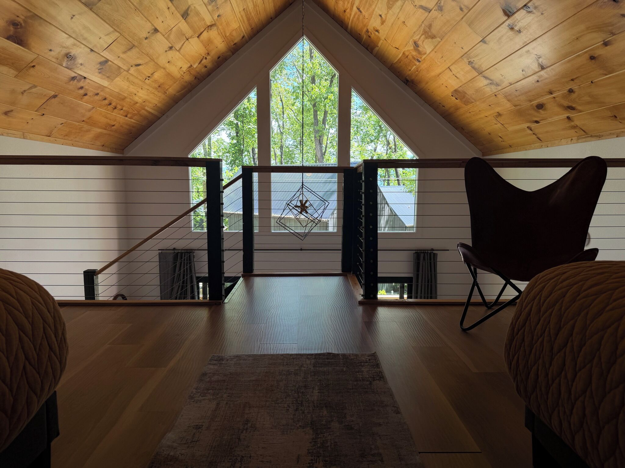 Dormitorio estilo loft con techo inclinado, vigas de madera, un ventanal grande, un adorno mural geométrico y una silla negra.