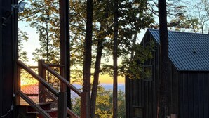 A wooden cabin with a staircase leading to a deck, surrounded by trees and a view of the sunset. - Summer Escape | Hot Tub (Sevierville)