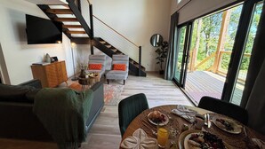 A modern living space with a staircase, seating area, dining table with breakfast, and large windows. - Summer Escape | Hot Tub (Sevierville)
