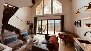 A spacious living room with a high ceiling, a staircase, a dining area, and a kitchen with a large window. - Summer Escape | Hot Tub (Sevierville)