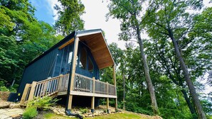 A cabin with a wooden deck and a large window, surrounded by trees. - Summer Escape | Hot Tub (Sevierville)