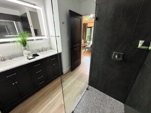 A modern bathroom with a glass shower enclosure, dark cabinetry, and a marble countertop.
