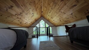 A loft bedroom with wooden slats on the ceiling, two beds, a large window, and a view of trees. - One Last Summer Getaway -1 (Sevierville)