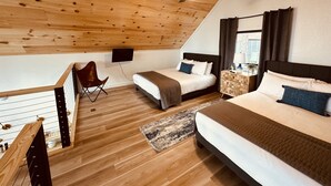 Une chambre avec un plafond en pente, un plancher en bois, un lit, une table de chevet avec une lampe, une chaise et un téléviseur fixé au mur.