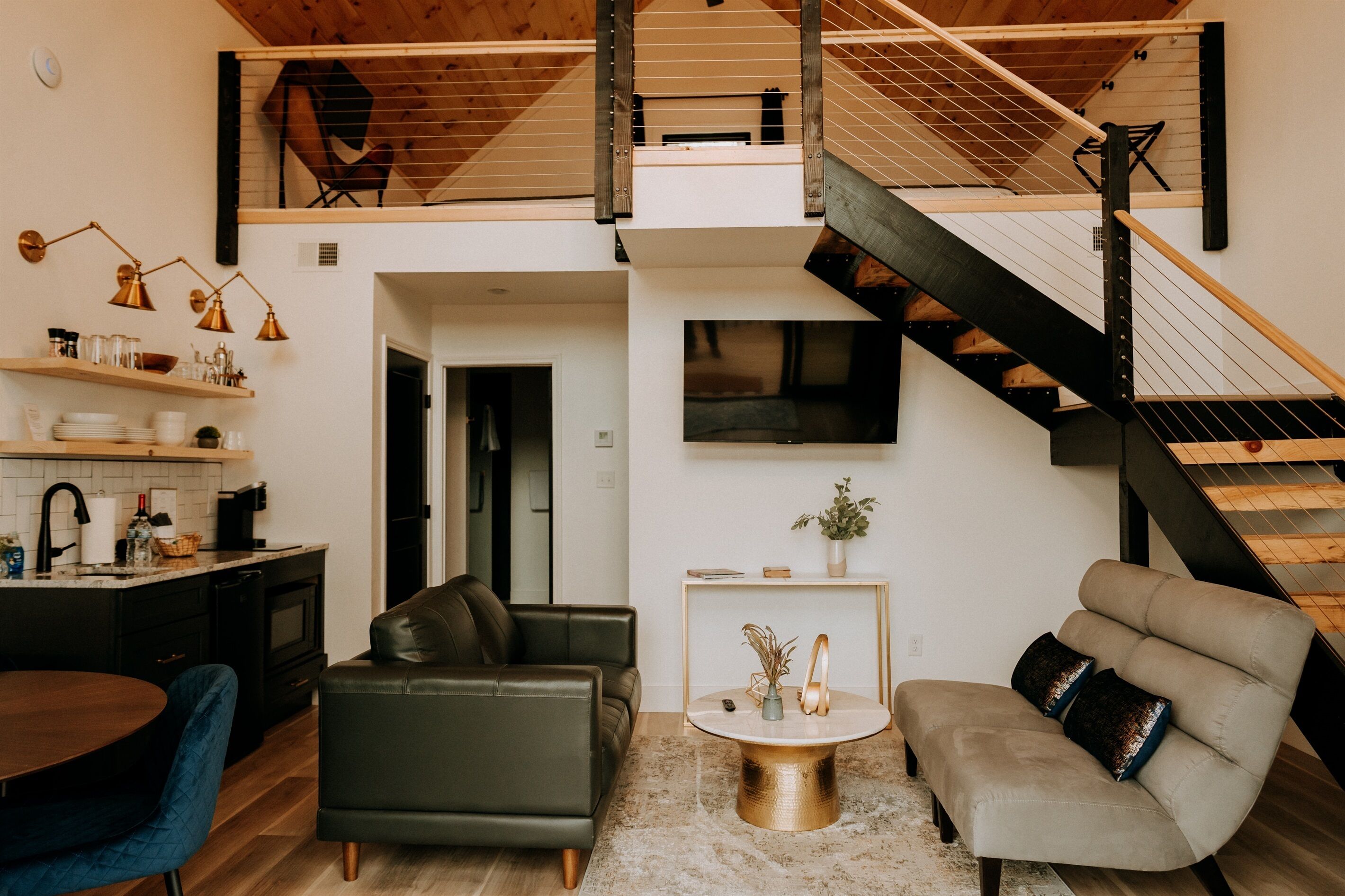 A modern loft-style living space with a kitchen, dining area, and a staircase leading to an upper level.