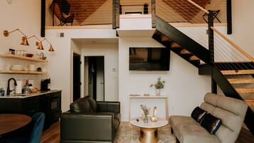 A modern loft-style living space with a kitchen, dining area, and a staircase leading to an upper level.