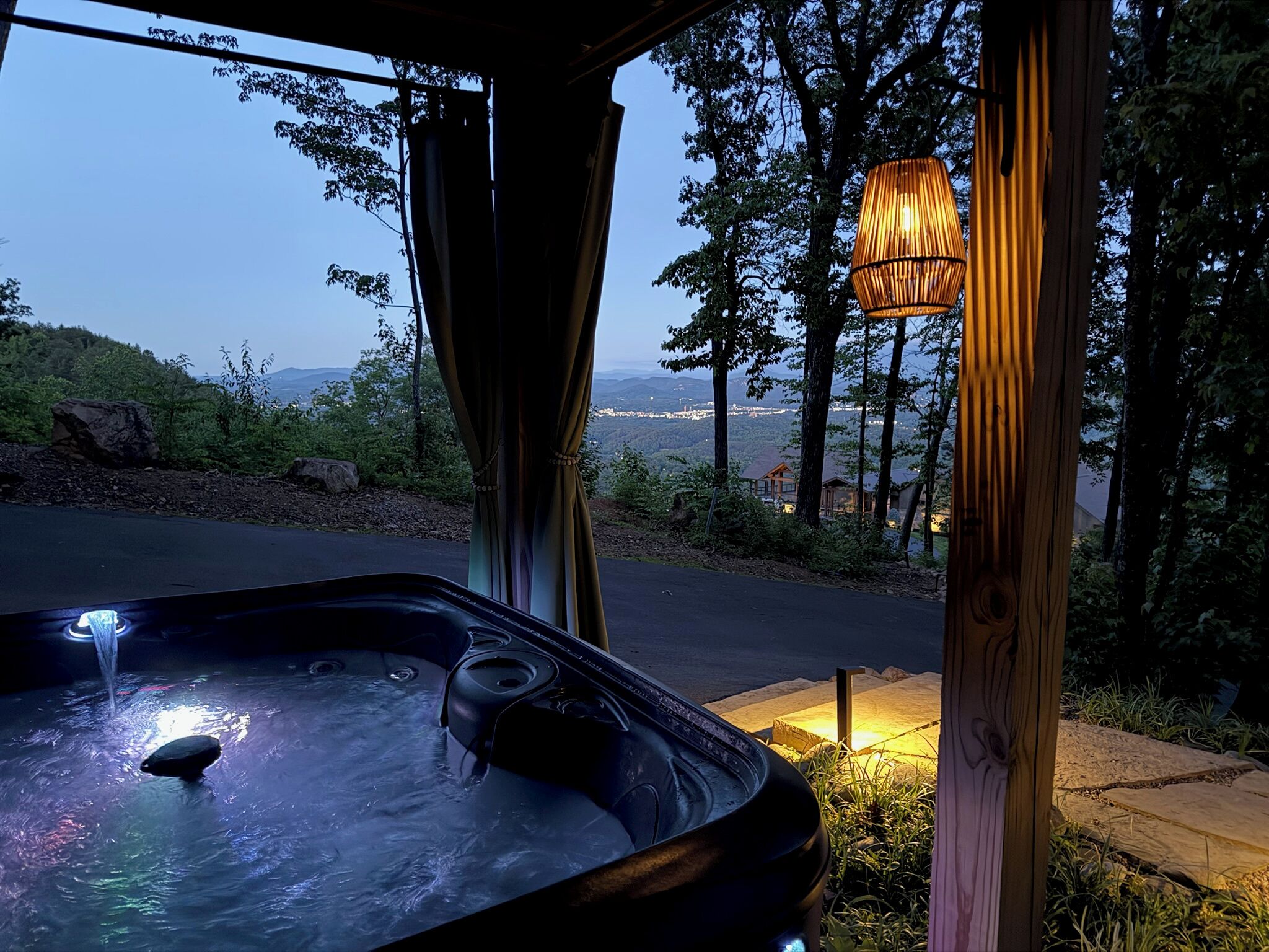 Un jacuzzi con vistas a un paisaje montañoso, una pérgola de madera y un colgador de luz.