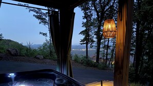 Ein Whirlpool mit Blick auf eine gebirgige Landschaft, eine Holz-Pergola und eine hängende Leuchte.