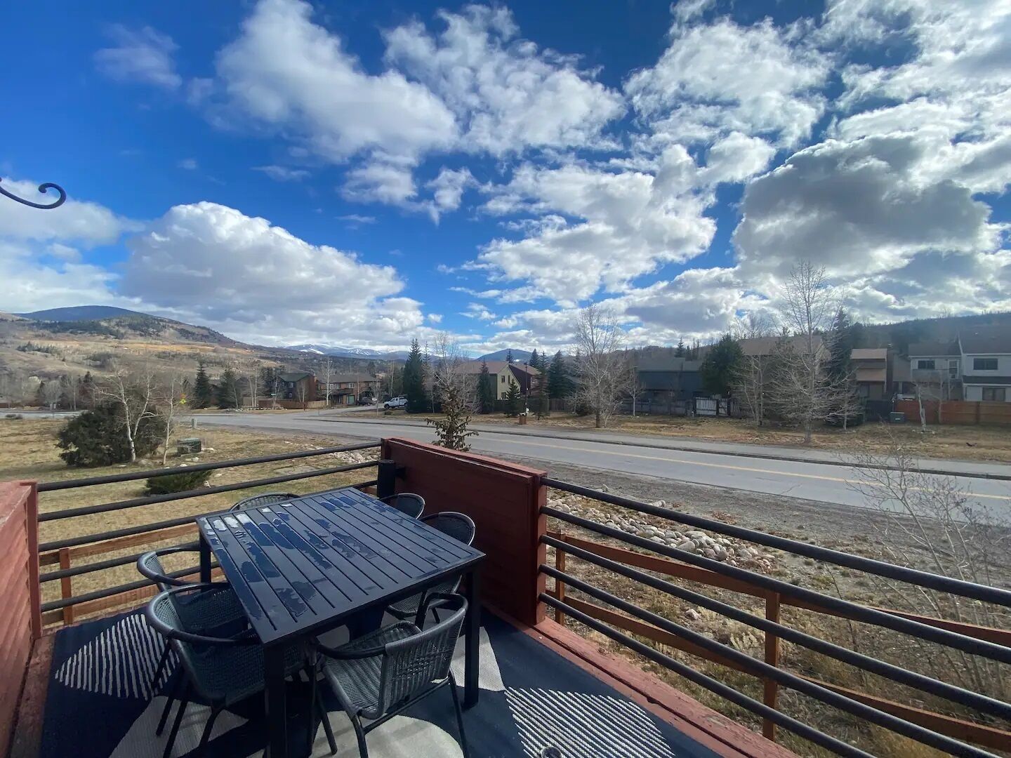 A balcony with a table and chairs, overlooking a road and distant mountains.