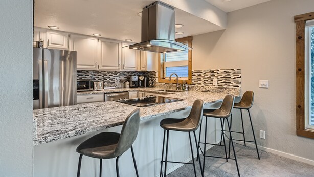 Una cocina moderna con un refrigerador de acero inoxidable, horno empotrado, una isla grande con taburetes de bar y vistas al exterior a través de una ventana.