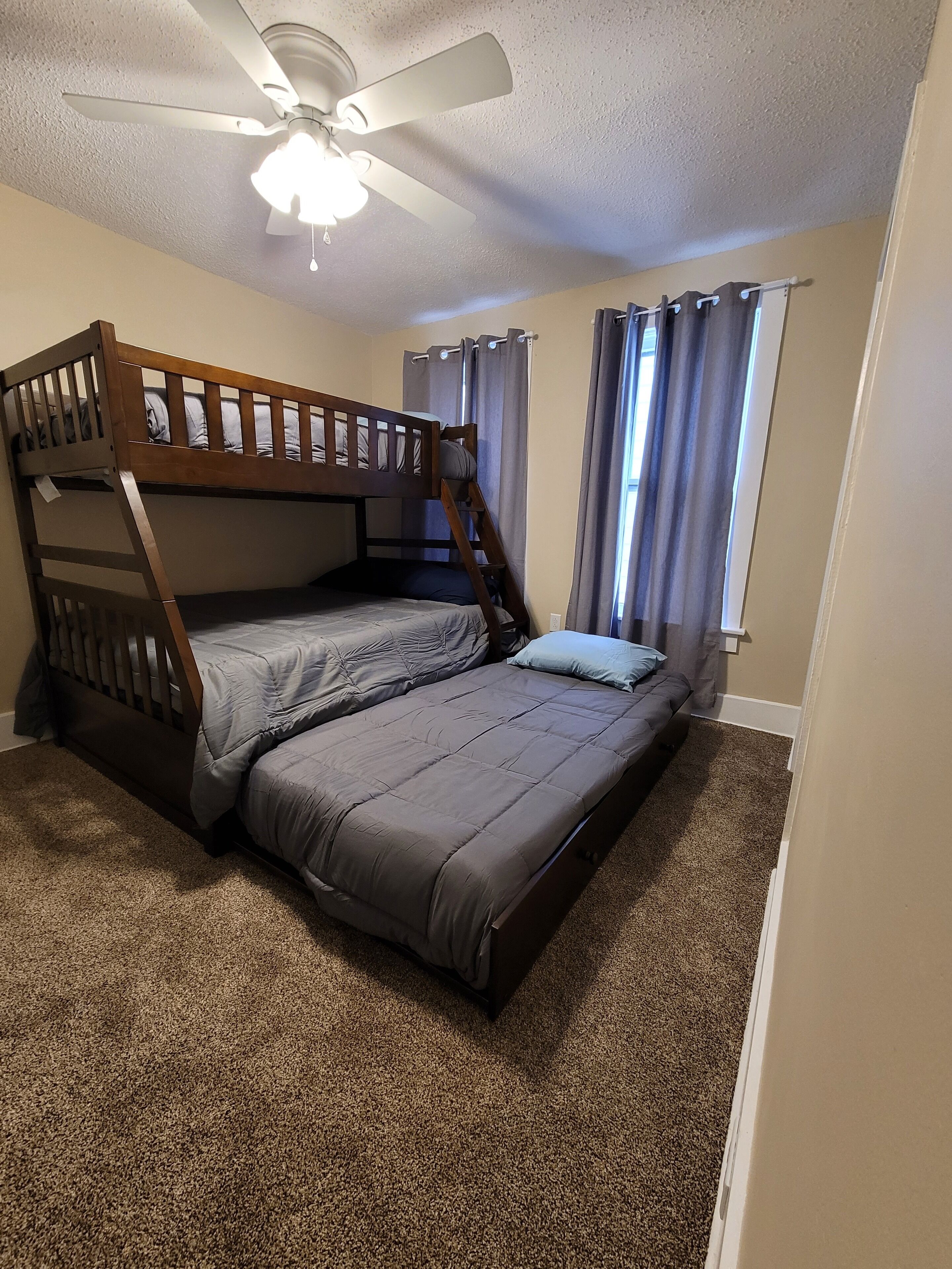 A bunk bed room with a ceiling fan, a window with curtains, and carpeted flooring.