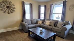 A living room with a sectional sofa, a coffee table, and a decorative wall piece. - 5-Mins to Cedar Point, 4-bedroom house. (Sandusky)