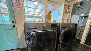 A laundry room with two front-loading LG washers, a window with a view of trees, and a sign stating "Children must have adult supervision." - Charming Bungalow On Main St & the Swamp Rabbit Trail with Private Pool (Travelers Rest)