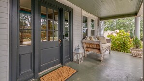 A porch with a dark door, a bench, and a small lantern. - Charming Bungalow On Main St & the Swamp Rabbit Trail with Private Pool (Travelers Rest)
