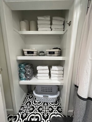 Un armario con repisas que contiene toallas dobladas y cestos de ropa con las etiquetas 'STUFF' y 'HOME'.
