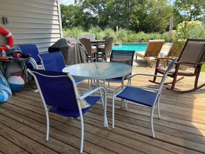 A deck with outdoor furniture, including chairs and a table, near a swimming pool.