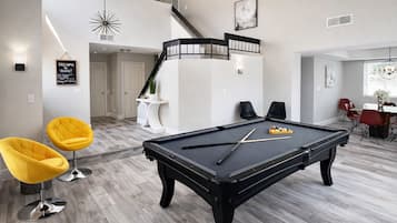 Een moderne woonkamer met een pooltafel, twee gele stoelen, en een trap naar een hoger gelegen niveau.