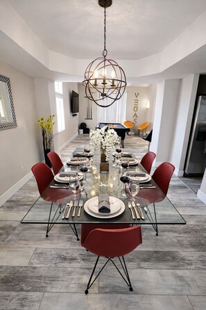 A dining area with a glass table, red chairs, and a modern chandelier. - 5 BR! Amazing Pool & Spa Retreat 15 Min to Strip (Henderson)