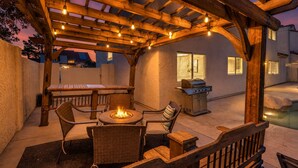 An outdoor patio with a pergola, a fire pit, a grill, and a pool.
