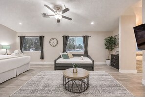 A modern bedroom with a bed, bedside table, lamp, clock, and a ceiling fan. - 5 BR! Amazing Pool & Spa Retreat 15 Min to Strip (Henderson)