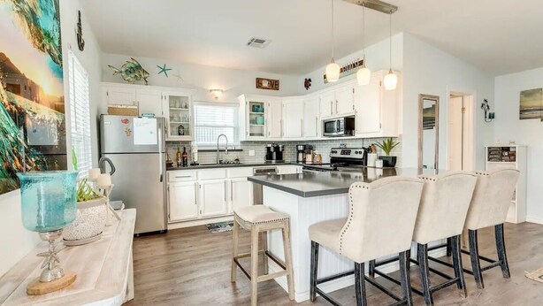 A modern kitchen with white cabinets, a central island with bar stools, a microwave, and a coffee machine.