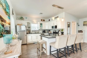 A modern kitchen with white cabinets, a central island with bar stools, a microwave, and a coffee machine.