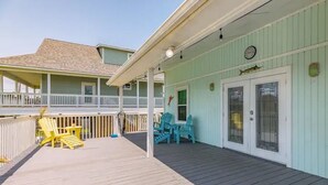 A covered deck with outdoor seating and a view of a house with a balcony.