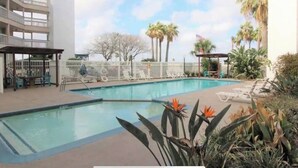 Ein Pool mit Liegestühlen und einer überdachten Sitzgelegenheit, umgeben von Palmen und einem mehrstöckigen Gebäude.