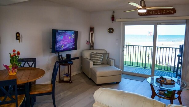 A living room with a TV, a dining table, a sofa, and a balcony with a view of the ocean. - Ocean Views surrounded by parks & secluded beaches (Flagler Beach)