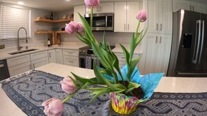 A modern kitchen with white cabinets, a stainless steel refrigerator, and a vase with pink tulips on the island. - Ocean Views surrounded by parks & secluded beaches (Flagler Beach)