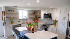 A modern kitchen with white cabinets, a central island with chairs, a microwave, and a refrigerator. - Ocean Views surrounded by parks & secluded beaches (Flagler Beach)