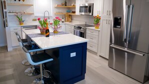 A modern kitchen with white cabinets, a stainless steel refrigerator, a built-in microwave, and a central island with bar stools. - Ocean Views surrounded by parks & secluded beaches (Flagler Beach)