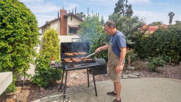 A man grilling food outdoors with a barbecue grill and a bottle of sauce.