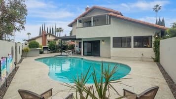 A residential property with a swimming pool, a covered patio, and a two-story house with a red-tiled roof.