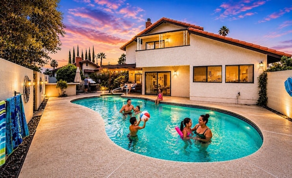Une piscine avec des gens, une maison et un ciel au coucher du soleil.