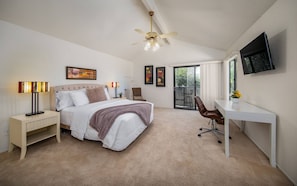 A bedroom with a bed, bedside tables, a desk, a chair, a ceiling fan, and a TV.