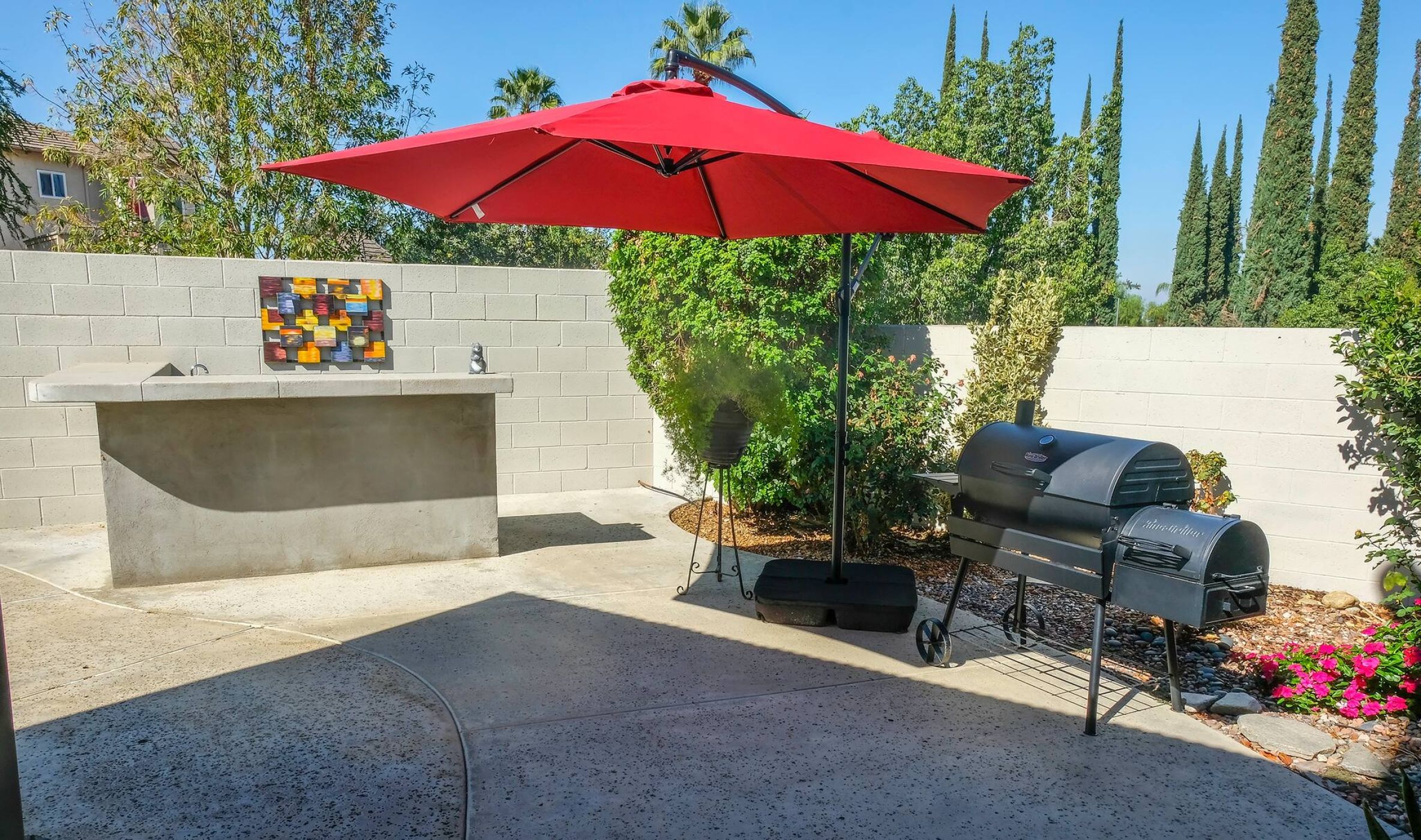 Eine Terrasse im Freien mit einem Grill, einem roten Sonnenschirm und einer Zierwand.
