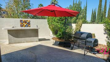 Eine Terrasse im Freien mit einem Grill, einem roten Sonnenschirm und einer Zierwand.