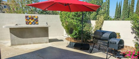 An outdoor patio with a barbecue grill, a red umbrella, and a decorative wall.